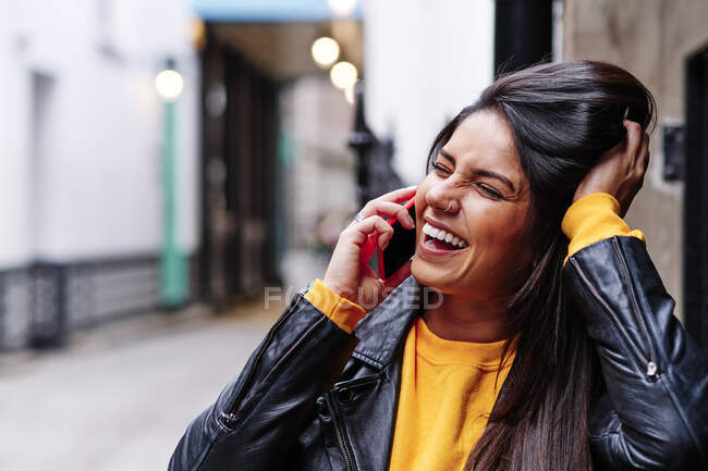 Cheerful young woman squinting while talking on mobile phone in city — Stock Photo