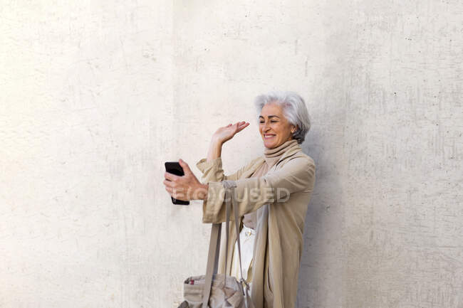 Glücklich reife Frau mit Einkaufstasche winkt Hand während Videoanruf — Stockfoto