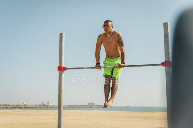 Shirtless male athlete exercising on high bar at beach — Stock Photo