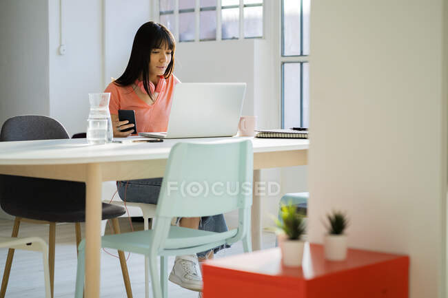 Mujer de negocios con teléfono inteligente utilizando el ordenador portátil en la oficina en casa - foto de stock