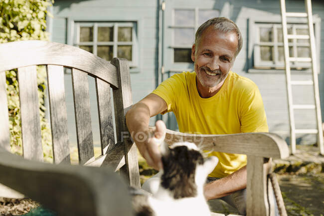 Усміхнена людина гладить кота на кріслі на задньому подвір'ї. — стокове фото