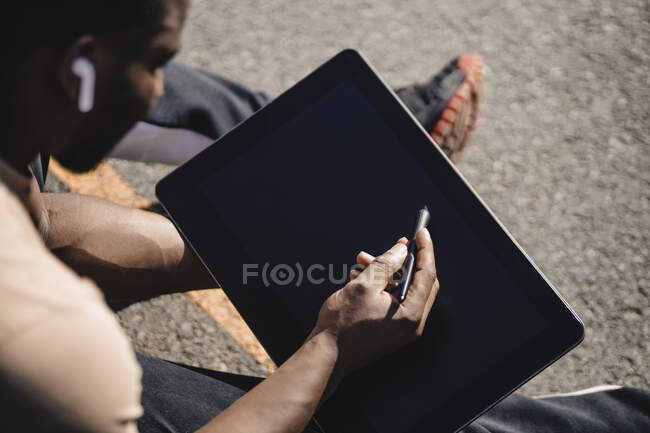 Junger Mann bedient Tablet durch digitalen Stift, während er auf Sportgericht sitzt — Stockfoto