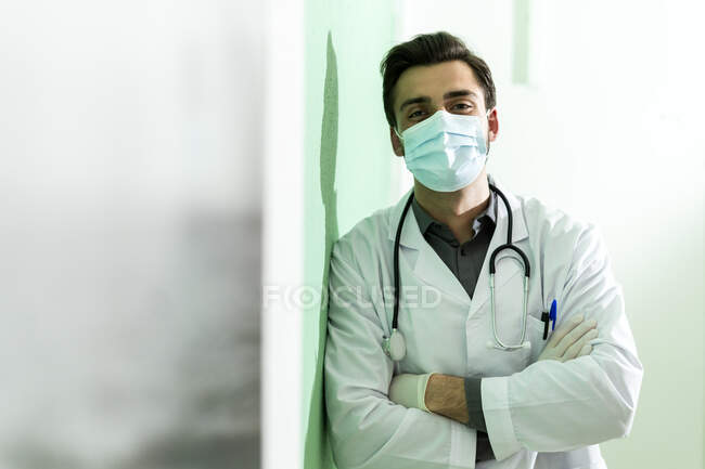 Homme travailleur de la santé portant un masque protecteur debout avec les bras croisés appuyé sur le mur — Photo de stock