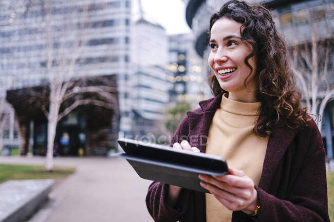 Sonriente mujer profesional sosteniendo tableta digital mientras mira hacia otro lado - foto de stock