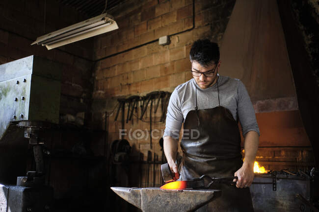 Handwerker schlägt in Werkstatt auf überhitztes Metall auf Amboss — Stockfoto