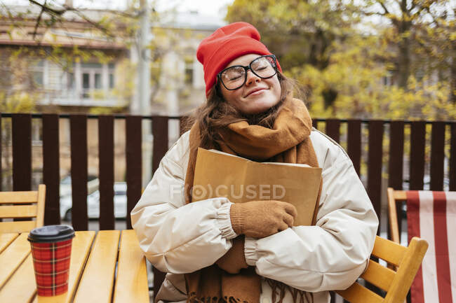 Woman in warm clothing embracing book while sitting at cafe — Stock Photo