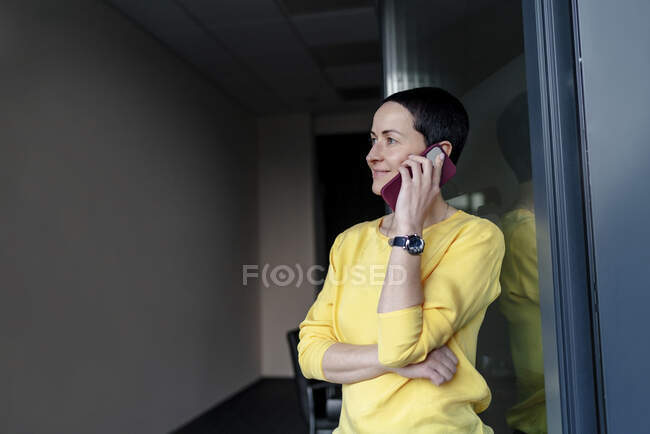 Sorridente donna d'affari contemplando mentre parla su smart phone in ufficio moderno — Foto stock