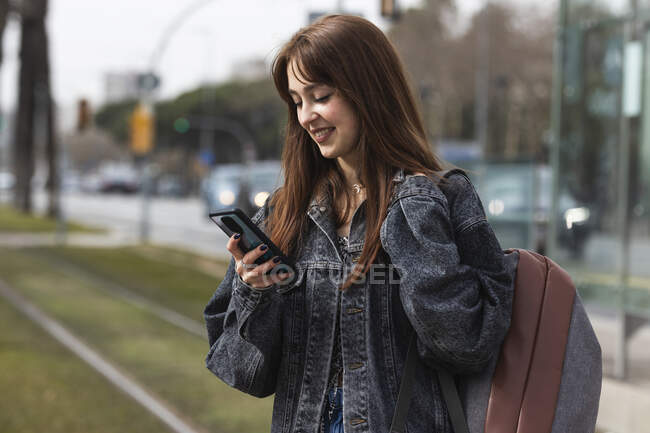 Femme souriante utilisant un téléphone intelligent tout en se tenant à la station de tram — Photo de stock