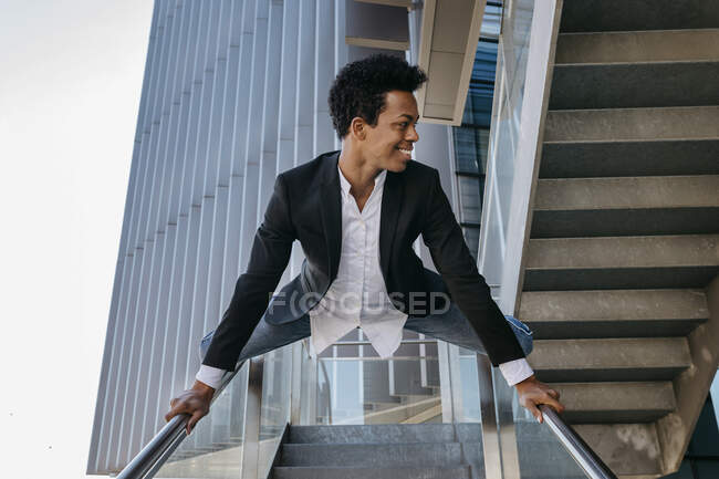 Lächelnder flexibler Geschäftsmann macht Spagat am Treppengeländer — Stockfoto