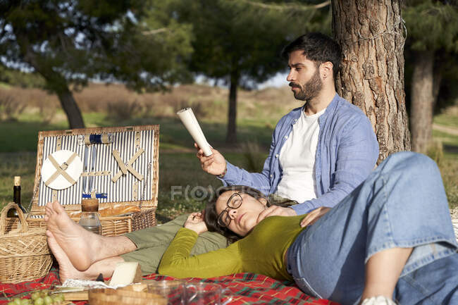 Donna rilassante mentre il fidanzato legge il libro sulla coperta durante il picnic — Foto stock