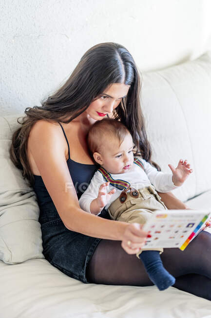 Jovem mãe mostrando livro para menino enquanto sentado na cama em casa — Fotografia de Stock