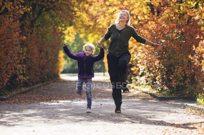Мать и дочь держатся за руки и бегают в парке осенью — стоковое фото