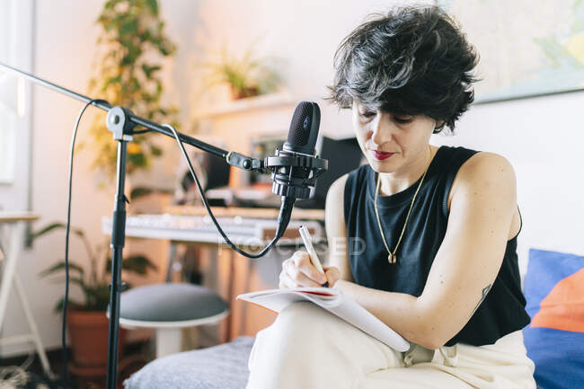 Жіночий музичний композитор пише у блокноті під час запису в студії. — стокове фото