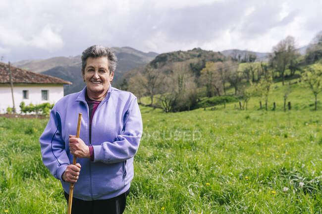 Lächelnde rüstige Seniorin steht mit Gehstock im Gras — Stockfoto