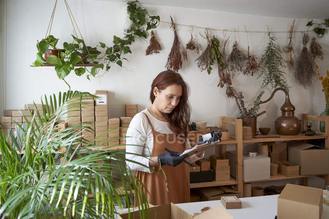 Female entrepreneur checking product on clipboard at workshop — Stock Photo