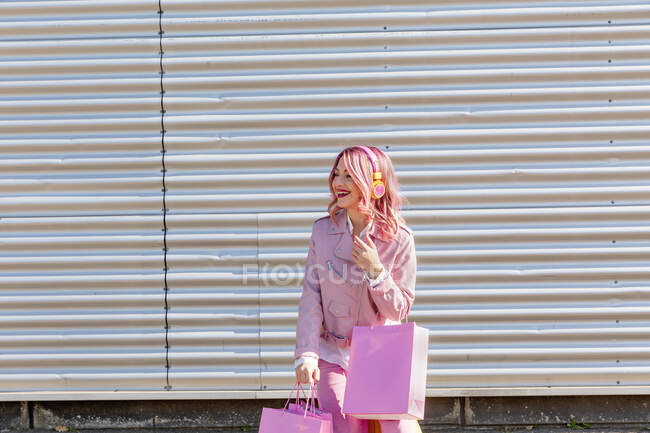 Mujer joven feliz con bolsas compras color rosa de pie frente a la pared corrugada — Millennials, Ocio - Stock Photo | #490872664