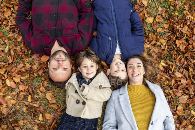 Smiling family lying on fallen leaf in forest during autumn — Stock Photo