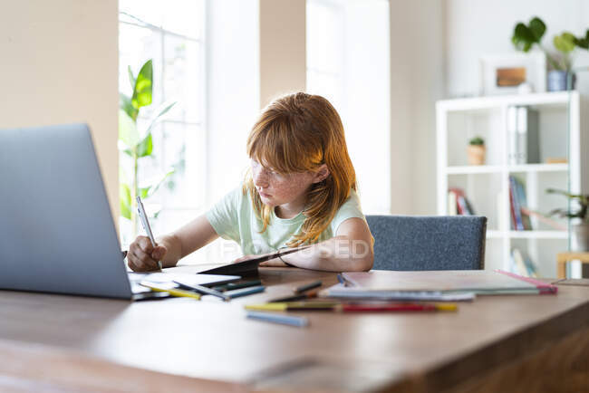 Зосереджена руда дівчина робить домашнє завдання перед ноутбуком. — стокове фото