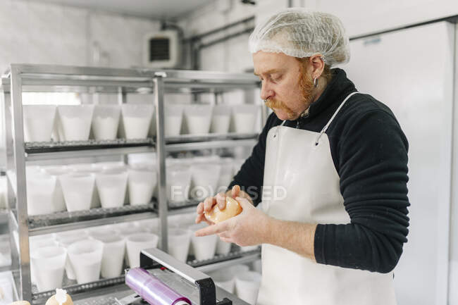 Chef masculino vestindo avental verificando queijo na sala de armazenamento — Fotografia de Stock