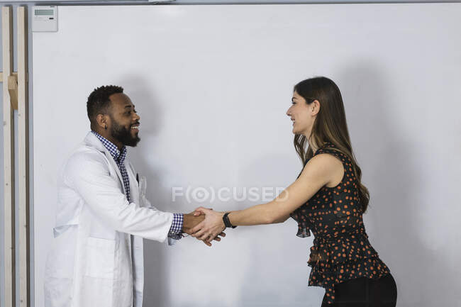 Sonriente saludo profesional médico masculino paciente femenina en la clínica - foto de stock