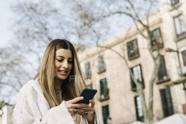 Посмішна жінка користується мобільним телефоном у місті. — стокове фото