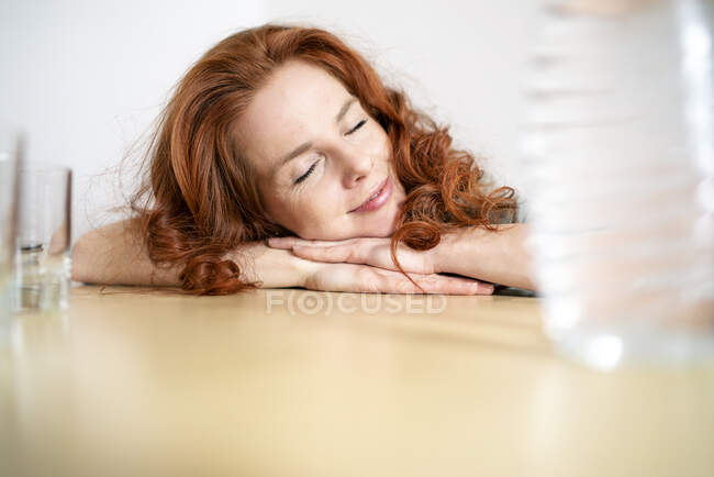 Mulher ruiva dormindo enquanto se inclina na mesa em casa — Fotografia de Stock