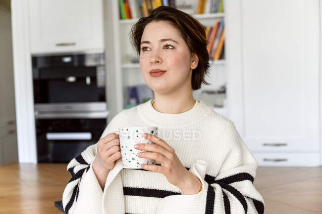 Mulher bonita segurando xícara de café enquanto olha para longe — Fotografia de Stock