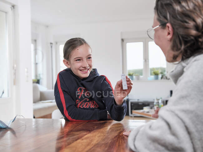 Посмішка дівчина показує негативний тест COVID-19 матері вдома — стокове фото