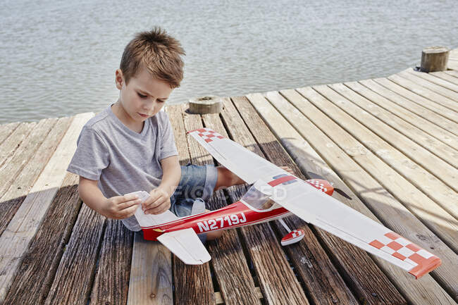 Ragazzo controllando giocattolo aereo mentre seduto sul molo — Foto stock