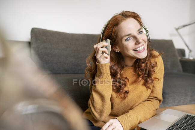 Smiling beautiful woman wearing headphones while sitting by laptop on coffee table at home — Stock Photo