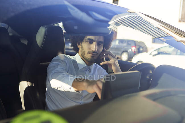 Businessman using GPS while talking on smart phone in car seen through windshield — Stock Photo