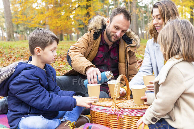 Чоловік наливає каву в чашку, сидячи з сім'єю в лісі — стокове фото