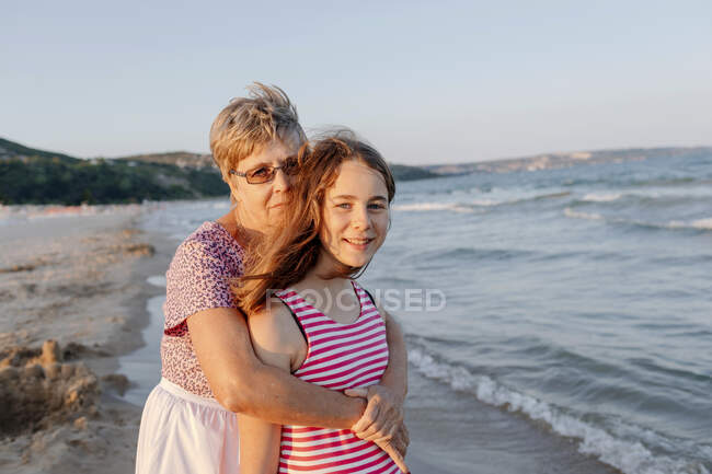 Mulher sênior abraçando neta enquanto estava na praia — Fotografia de Stock