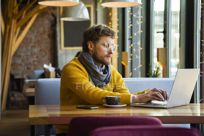 Hombre propietario trabajando en el ordenador portátil mientras está sentado en la cafetería - foto de stock