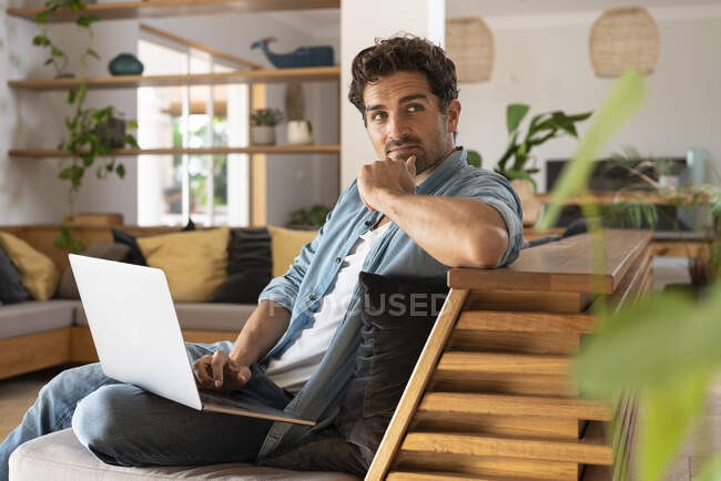 Pensiero lavoratore freelance maschile guardando lontano mentre seduto con il computer portatile sul divano — Foto stock