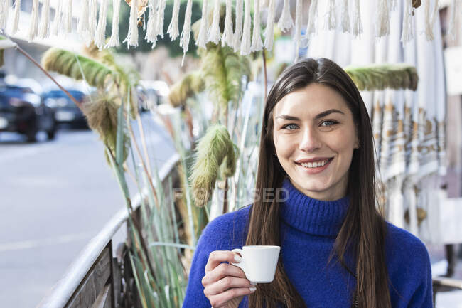 Lächelnde schöne Frau mit grauen Augen hält Kaffeetasse gegen Pflanze — Stockfoto