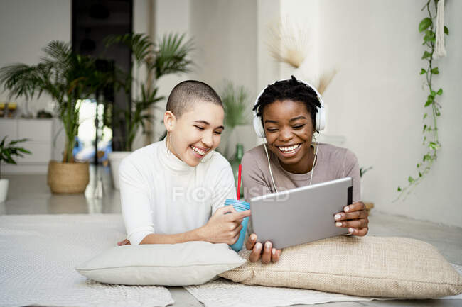 Joyeuses collègues féminines qui utilisent une tablette numérique alors qu'elles sont allongées devant dans le salon — Photo de stock