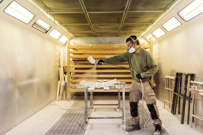 Männlicher Tischler sprüht Farbe auf Holzmaterial in Spritzkabine — Stockfoto