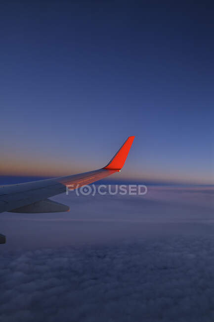 Ala de avião comercial voando contra o céu ao entardecer — Fotografia de Stock