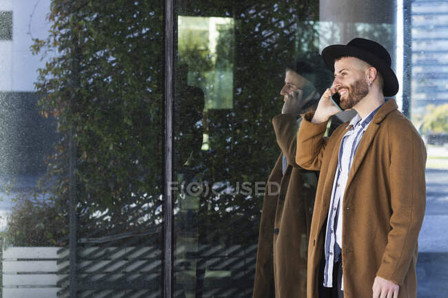 Homme d'affaires adulte moyen parlant sur un téléphone portable tout en se tenant près d'un mur de verre — Photo de stock
