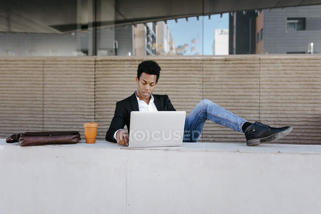 Geschäftsmann mit hochgezogenen Füßen mit Laptop an Stützmauer — Stockfoto