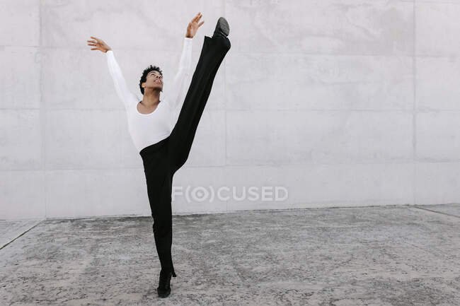 Гнучка чоловіча танцівниця дивиться вгору, розтягуючи ногу на стіну — стокове фото