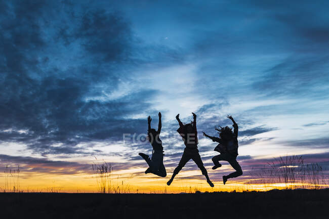 Amigas despreocupadas con los brazos levantados saltando frente al cielo - foto de stock