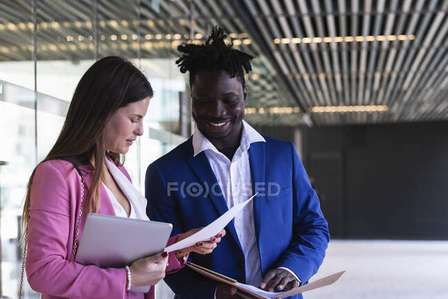 Young businesswoman checking paper while standing by coworker at office corridor — Stock Photo