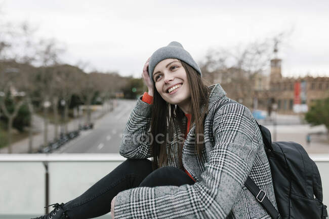 Задумчивая улыбающаяся женщина сидит на улице в городе — стоковое фото