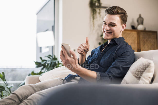 Uomo sorridente gesticolando pollici in su mentre fa videochiamata attraverso smart phone — Foto stock