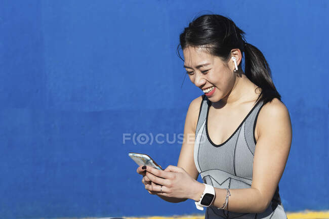 Smiling woman using mobile phone against blue wall — Stock Photo