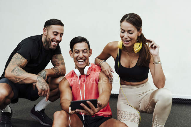 Sportivo ridente che usa il cellulare con gli amici in palestra — Foto stock