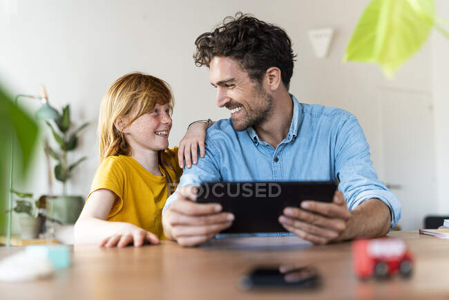Отец с цифровой планшет улыбается дочери, сидя дома — стоковое фото