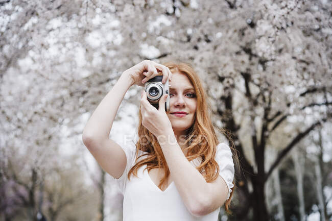 Молода руда жінка фотографує через камеру в парку — стокове фото